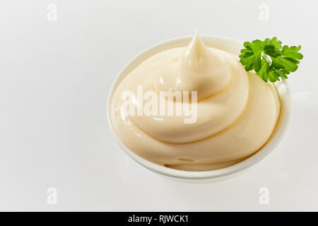 Small bowl of twirled spicy mayonnaise garnished with a leaf of fresh parsley high angle on white with copy space Stock Photo