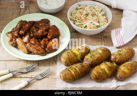 American chicken wings, hasselback potatoes with sauce and coleslaw on a wooden background. Rustic style. Stock Photo
