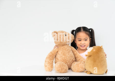 Young lovely Asian girl playing with 2 cute teddybear dolls at home, copy space on white wall background. Child's play, youth childhood activity Stock Photo