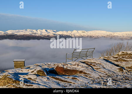 A seat with a view. Far-reaching views above the cloud inversion of the snow-covered fells from Orrest Head near Windermere Stock Photo