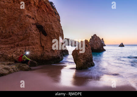 Man sitting by cliff at sunset, wearing illuminated headlamp, Alvor, Algrave, Portugal, Europe Stock Photo
