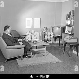 Television in the 1950s. A proud elderly man is pictured in his home with his wife with the latest in electronic home equipment visible. A typical television set on thin legs, a radio and a tape recorder.  Photo Kristoffersson ref CD88-10. Sweden 1959 Stock Photo