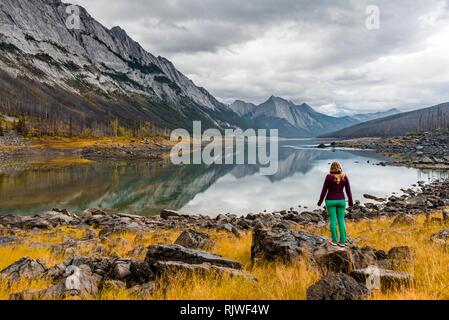 Young woman standing on a rock, looking into the landscape, mountains reflected in a lake, Medicine Lake, Maligne Valley Stock Photo