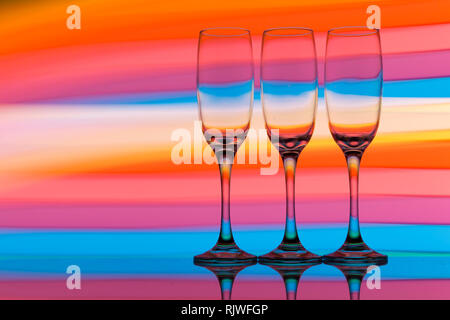 Three champagne glasses in a row with a rainbow of colorful light painting behind them Stock Photo