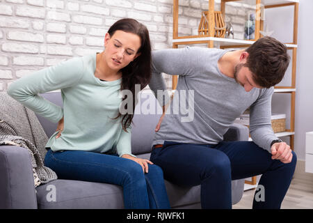 Sad Couple Sitting On Sofa Suffering From Backache Stock Photo