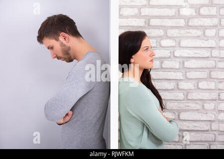 Side View Of Young Unhappy Couple Standing Back To Back At Home Stock Photo