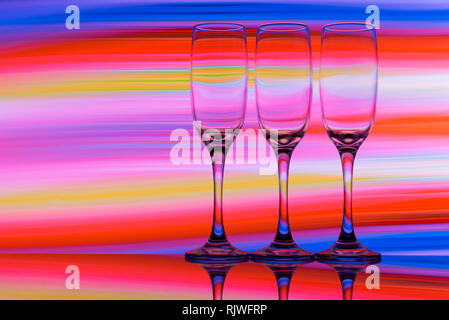 Three champagne glasses in a row with a rainbow of colorful light painting behind them Stock Photo