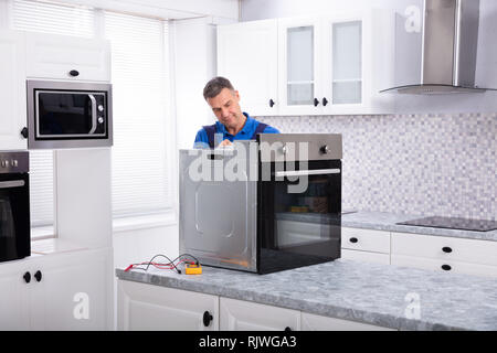 Mature Male Technician Repairing Oven On Kitchen Worktop Stock Photo