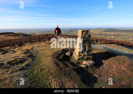 Walker at the OS Trig Point at the summit Cairn of Ling Fell, Wythop Moss, Lake District National Park, Cumbria, England, UK Stock Photo