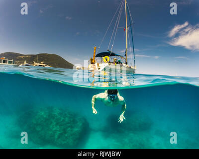 Split level photo of a Man swimming in clear blue sea with a yacht in