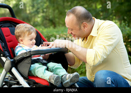 outdoor portrait of a happy father and son. baby sitting in stroller and dad walking in summer park Stock Photo