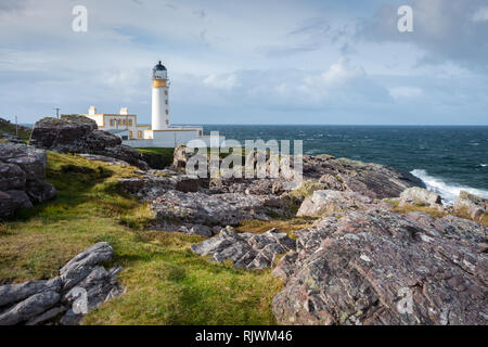Looking across rocks and grassland towards Rua Reidh lighthouse on a sunny and cloudy day at the entrance to Loch Ewe, Wester Ross, Scotland Stock Photo