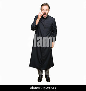 Middle age priest man wearing catholic robe afraid and shocked with surprise expression, fear and excited face. Stock Photo