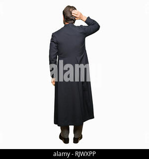 Middle age priest man wearing catholic robe Backwards thinking about doubt with hand on head Stock Photo