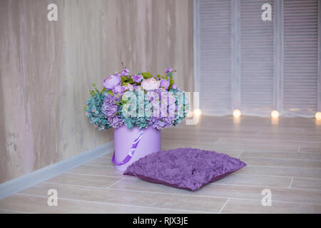Cozy modern home with decor inspired by designers and florist soul with royal violet colors. Purple pillow with composition with bucket of fancy flowe Stock Photo