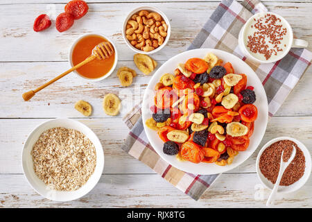 dried Fruits and Nut Mix bowl - banana slices, apricots, raisins, prunes, cherries and cashew on a rustic table with porridge, honey in a bowl and yog Stock Photo