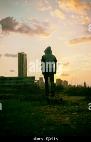 Rear view hooded male wealking towards the city Stock Photo