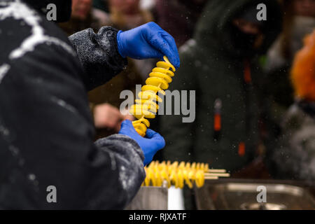 Man makes deep fried golden spiral potato on a wooden stick. Twist crispy crunchy take away street food Stock Photo