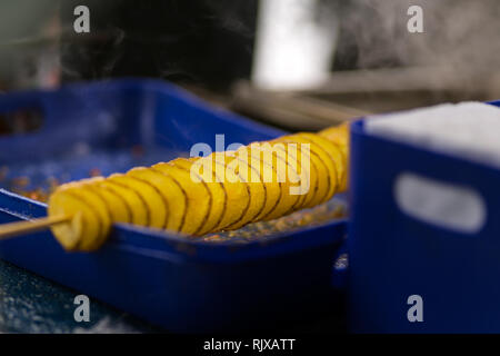 Man makes deep fried golden spiral potato on a wooden stick. Twist crispy crunchy take away street food Stock Photo