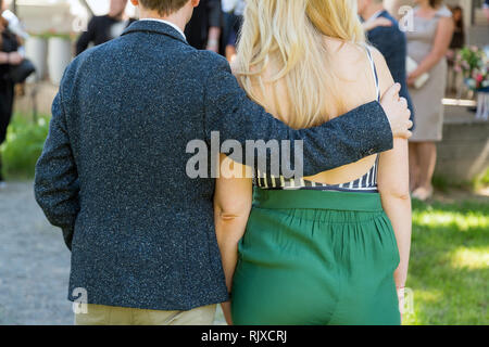 Happy young couple from behind, man is hugging his girlfriend while being in a wedding party Stock Photo