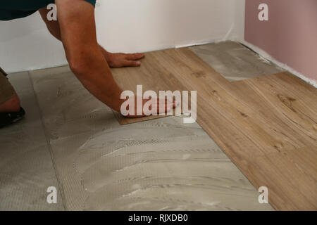 Work on laying flooring. Worker installing new vinyl tile floor. Stock Photo