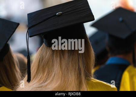 Students wearing gowns and hats sitting indoors, waiting to receive diplomas, graduation day in university, college commencement Stock Photo