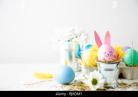 Cute easter background with an egg decorated as a rabbit in a flower pot, daisies and feathers Stock Photo