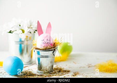 Cute easter background with an egg decorated as a rabbit in a flower pot, daisies and feathers Stock Photo