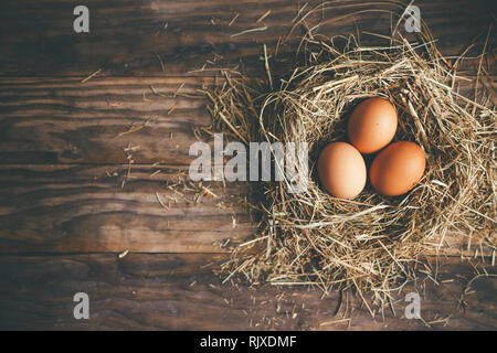 Fresh chicken eggs in hay nest on a rustic wooden background. Top view Stock Photo