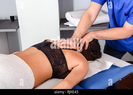 Male osteopath working on neck and shoulders, making massage to woman client Stock Photo