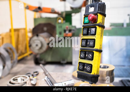 Crane remote control buttons in yellow case on wire. Lathe machine is blurred in background Stock Photo