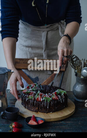 Woman is cutting a strawberry cake on the wooden table. Stock Photo