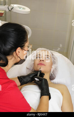 Girl in spa salon. Cosmetic procedure for rejuvenation. Facelifting. Cosmetologist makes collagen injections in area under lower lip. Stock Photo