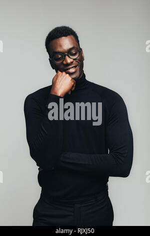 Happy young african man smiling with eyes closed against gray background. Man in black casuals standing with a pleased smile. Stock Photo