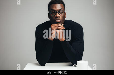 African man sitting at table and waiting for someone. Young guy at cafe table looking away and thinking. Stock Photo