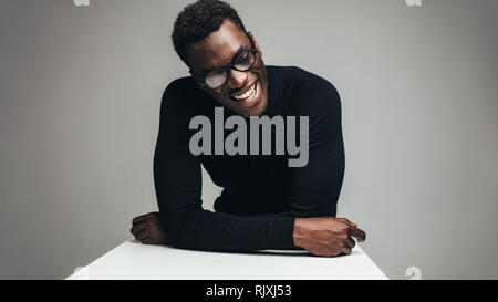African man sitting at table and smiling. Relaxed young guy against gray background. Stock Photo