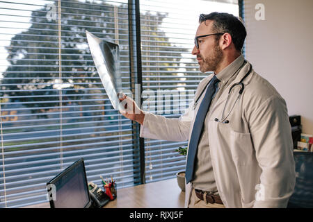 Mature male doctor looking at a radiography. Doctor looking at a x ray of his patient in his office. Stock Photo