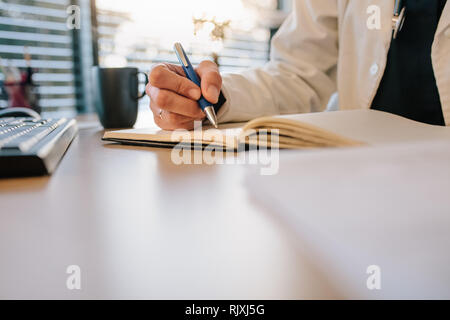 Close up of female doctor hands writing something on her diary. Female physician writing notes on patient in office. Stock Photo