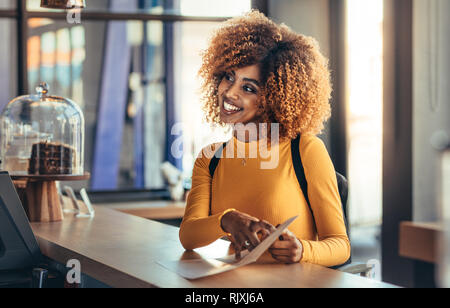 Smiling woman traveller showing the menu card to order food. Tourist woman wearing a backpack enquiring about food standing at the billing counter of Stock Photo