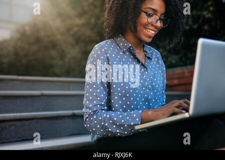 Woman sitting on steps outdoors and using laptop. businesswoman working on laptop while sitting on steps outside. Stock Photo