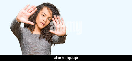 Young beautiful woman with curly hair wearing grey sweater Smiling doing frame using hands palms and fingers, camera perspective Stock Photo