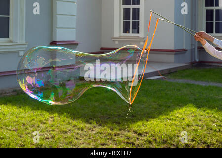 Man makes big soap bubbles while holding two sticks and thread in his hands outdoor on the grass Stock Photo