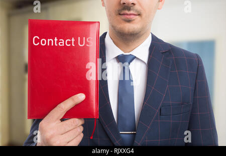 Businessman advertising communication services as holding with hand red notebook having contact us text on leather cover Stock Photo