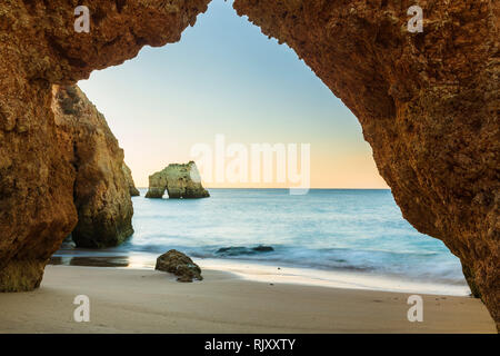 Looking through natural arch at of cliff at sunset over sea, Alvor, Algarve, Portugal, Europe