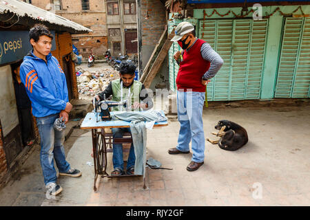 Kathmandu, Nepal - November 25, 2016: A man seamstress sews clothes on the streets of Kathmandu. Other men are watching his work. Stock Photo