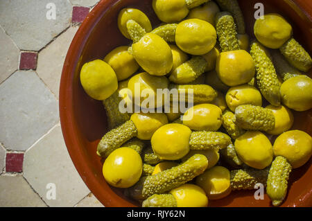 Pickled olives stuffed with gherkins served on clay bowl. Overhead shot over glazed tile mosaic table Stock Photo