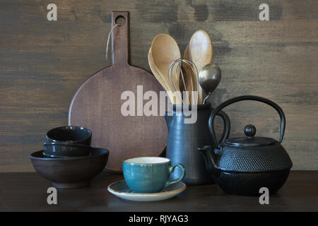 Crockery, clayware, dark utensils and other different stuff on wooden tabletop. Kitchen still life as background. Stock Photo