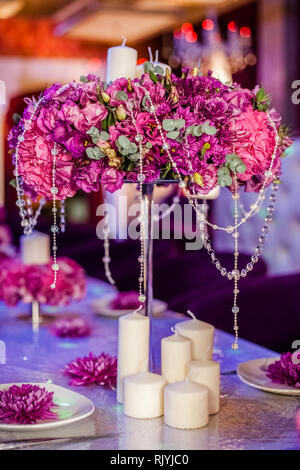 Wedding party table flowers and white candles on the table. Pink pions and wite chrysanthemums bouqet with shining decor. Stock Photo