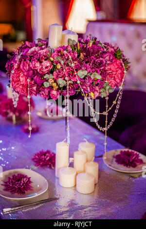 Wedding party table flowers and white candles on the table. Pink pions and wite chrysanthemums bouqet with shining decor. Stock Photo