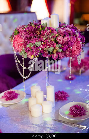 Wedding party table flowers and white candles on the table. Pink pions and wite chrysanthemums bouqet with shining decor. Stock Photo